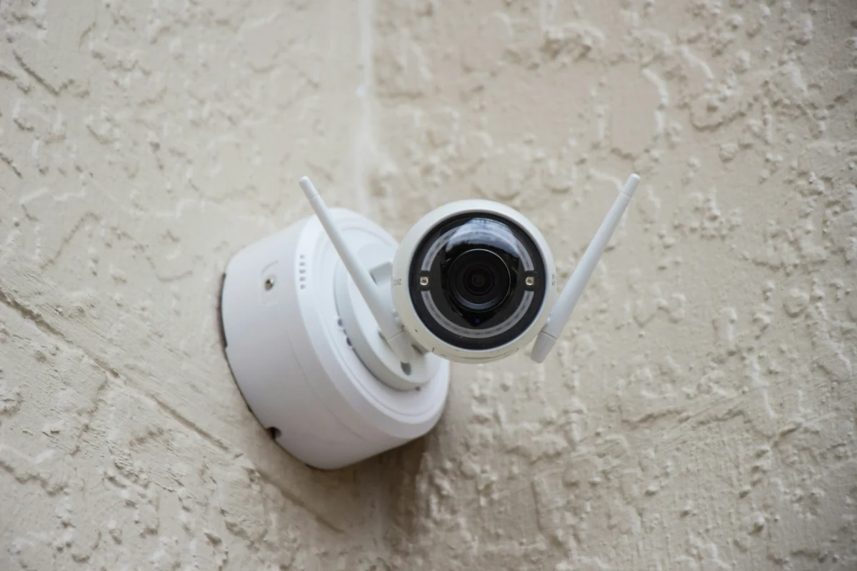 network-design-voip-img-2 White outdoor security camera mounted on a textured stucco wall, angled downward.