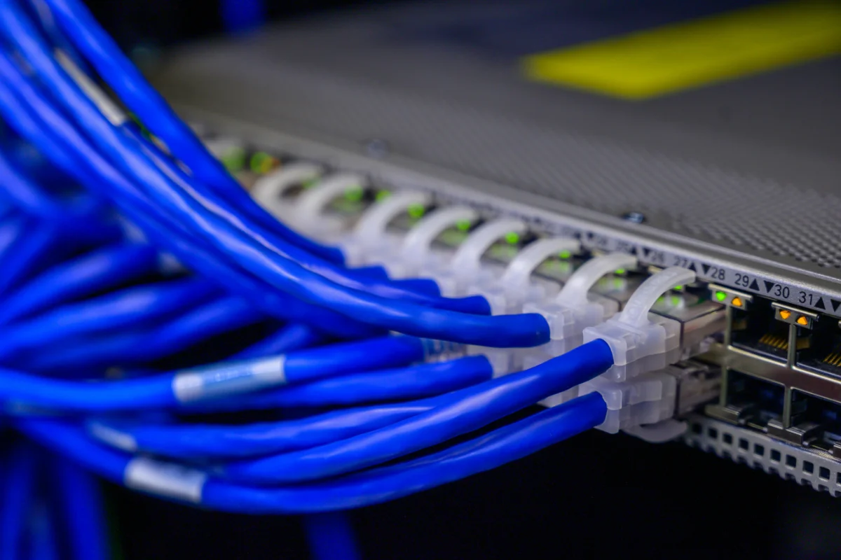 network-design-voip-img-3 Blue Ethernet cables plugged into a network patch panel with green status LEDs in a data center.